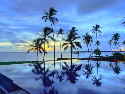 Ein ruhiger Pool mit Spiegelung von Palmen und blauem Himmel bei Sonnenuntergang am Meer.