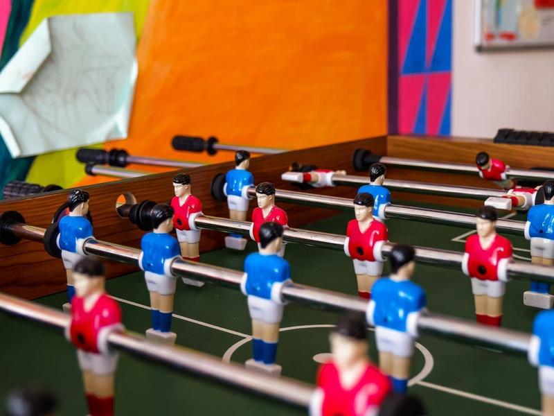Tischfußballspiel mit roten und blauen Spielfiguren vor bunter Wand.