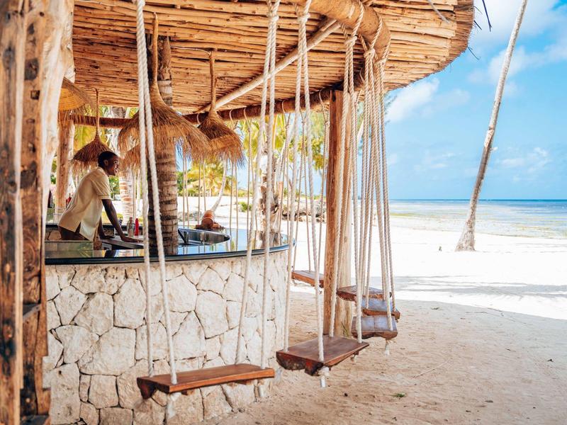 Strandbar mit Holzschaukeln, Sandboden und blauem Himmel am sonnigen Meer.