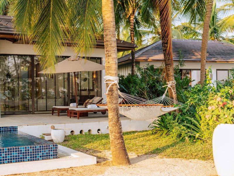 Moderner Garten mit Pool, Hängematte an Palme, Liegestühle und grüner Pflanzenkulisse.