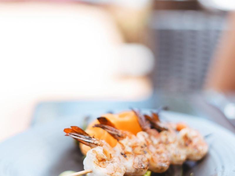 Gegrillte Garnelenspieße auf gemischtem Salat mit Avocado und orangenfarbener Sauce auf blauem Teller.
