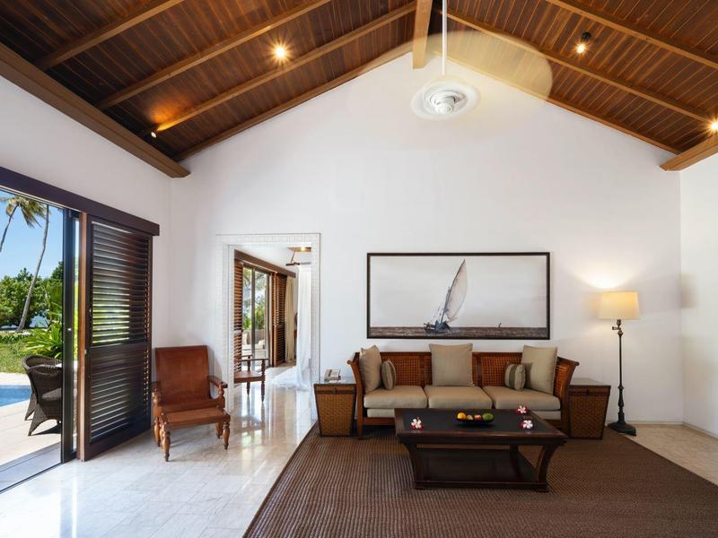 Helles Wohnzimmer mit Holzbalkendecke, braunem Sofa, großem Fenster und offenem Zugang zum Garten.