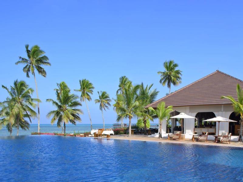 Infinity-Pool mit Palmen und einer offenen Strandbar unter blauem Himmel am Meer.