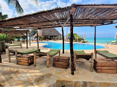 Strandbar mit Holzmöbeln, Palmen und Blick auf türkisfarbenes Meer bei sonnigem Himmel.