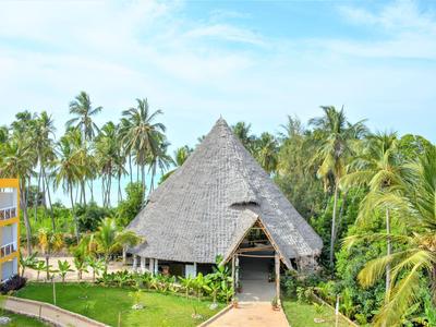 Groot rietgedekt gebouw naast hotel met palmbomen en zee op de achtergrond.