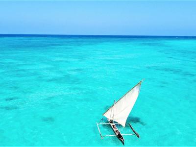 Ein kleines segelboot mit weißem segel auf klarem, türkisblauem wasser unter blauem himmel.