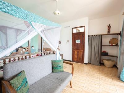 Helles Zimmer mit Holzsofa, Moskitonetz, Holztür, Vorhang und Kachelfußboden.