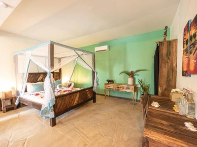 Helles Schlafzimmer mit vier Poster-Bett, grüner Wand, Holzmöbeln und freundlicher Dekoration.