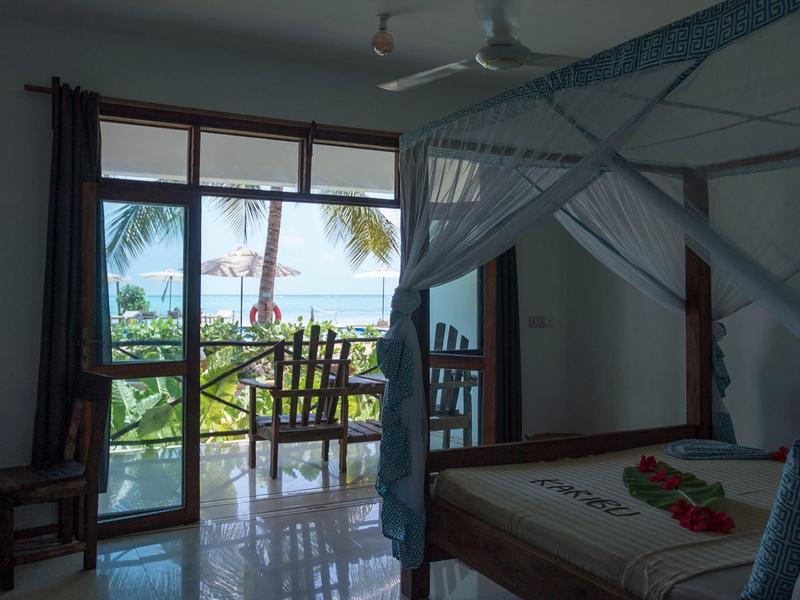 Zimmer mit Himmelbett öffnet sich zu Balkon mit Meerblick und Palmen bei Tageslicht.