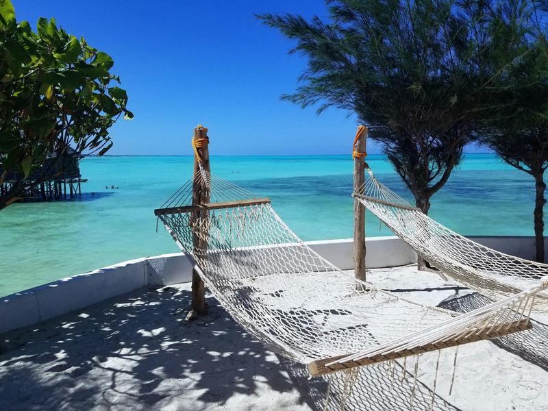 Zwei weiße Hängematten an Holzpfosten am weißen Sandstrand vor türkisblauem Meer und blauem Himmel.