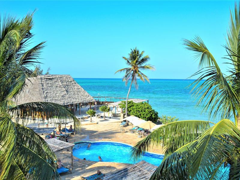 Tropisches Resort mit Pool, Palmen und Blick auf das blaue Meer unter klarem Himmel.