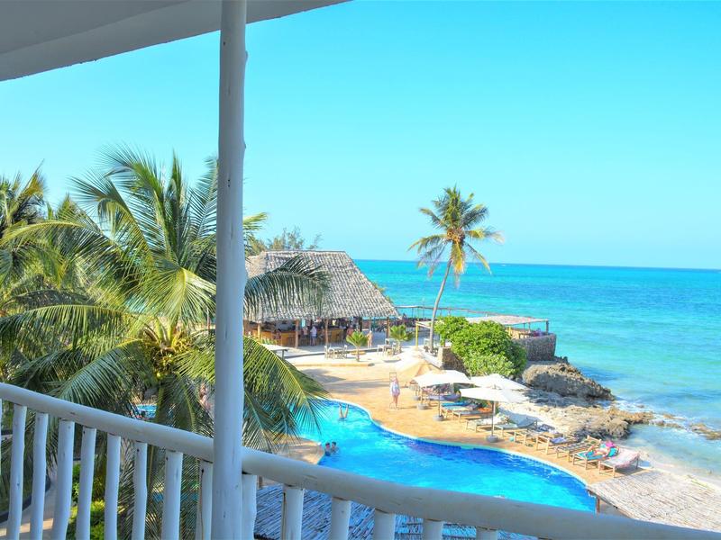 Meerblick mit blauem Pool, Sandstrand, Palmen und klarem Himmel im tropischen Urlaubsresort.