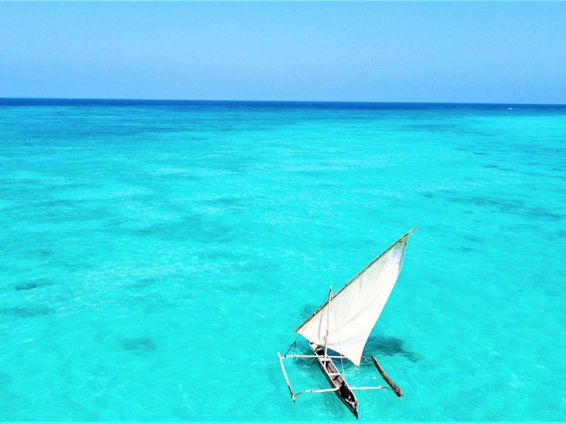 Ein kleines segelboot mit weißem segel auf klarem, türkisblauem wasser unter blauem himmel.
