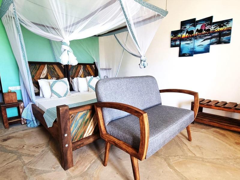 Schlafzimmer mit Holzmöbeln, Himmelbett, grauem Sofa, Hocker und Wandbild, heller Boden.