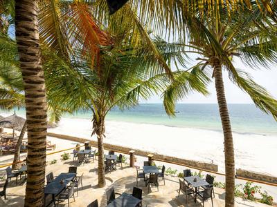 Strandterrasse mit Tischen, Stühlen und Palmen mit Blick auf den ruhigen Ozean.