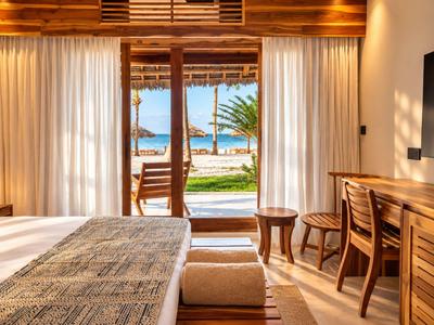 Chambre avec mobilier en bois et vue sur la mer à travers de grandes fenêtres avec rideaux.