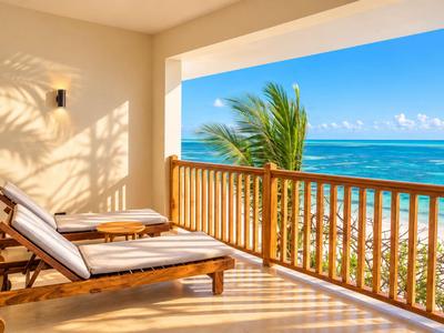 Balcon avec deux chaises longues donnant sur la mer et un palmier sous un ciel bleu.