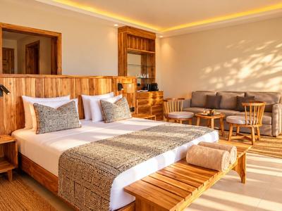 Chambre d’hôtel lumineuse avec lit double, mobilier en bois et coin salon à la lumière du jour.
