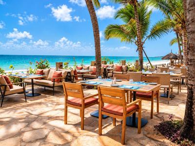 Restaurant en bord de mer avec tables en bois, chaises et palmiers.
