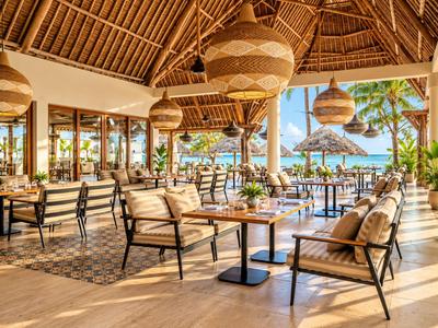 Espace ouvert d'hôtel avec chaises, tables et vue sur un environnement tropical et la mer.