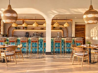 Espace bar d'hôtel lumineux avec tabourets turquoise, tables en bois et lampes décoratives.