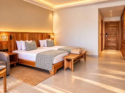 Chambre d'hôtel lumineuse avec grand lit, meubles en bois et lumière naturelle chaude.