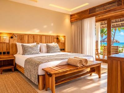 Chambre d'hôtel lumineuse avec lit double, meubles en bois et vue sur un paysage tropical.