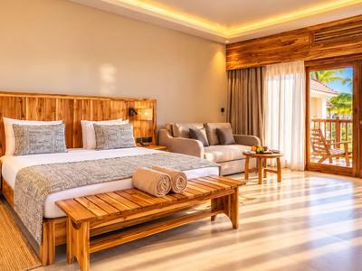 Chambre d'hôtel spacieuse avec mobilier en bois, lit confortable et balcon donnant sur des palmiers.