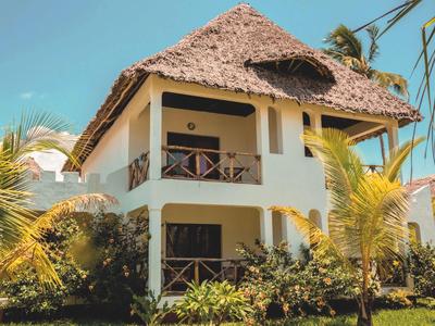 Zwei-Stock-Hotelgebäude mit Strohdach und Umgeben von Palmen und Grünflächen.