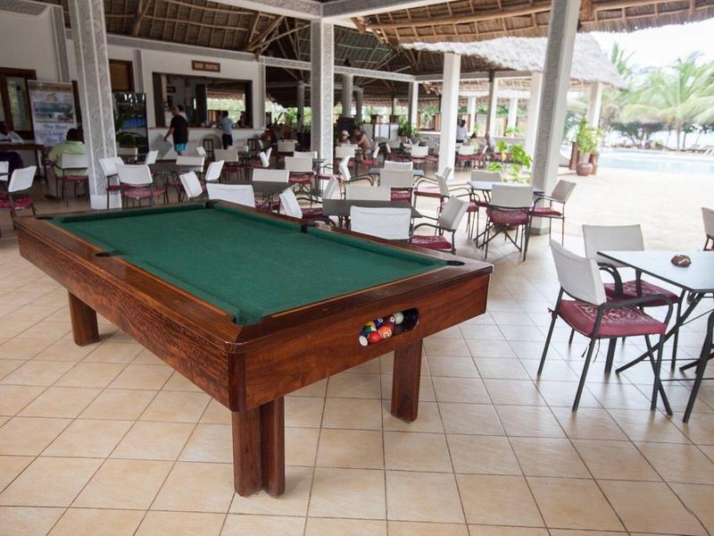 Billardtisch mit grünem Filz in hellem, offenem Gastraum mit Stühlen und Tischen auf Fliesenboden.