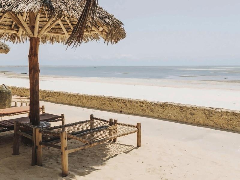 Leerer Strand mit Holzliegen und Strohdach am ruhigen Meer bei klarem Himmel.