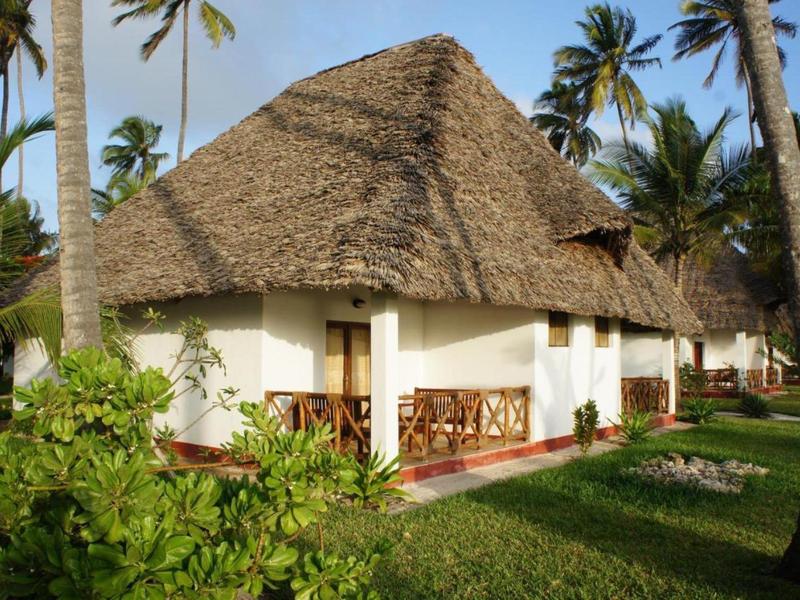 Weißes Haus mit strohgedecktem Dach umgeben von Palmen und grünem Gras.