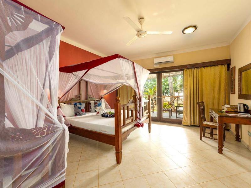 Geräumiges Schlafzimmer mit Holzbett, Moskitonetz, Schreibtisch und Zugang zu Balkon mit Pflanzen.