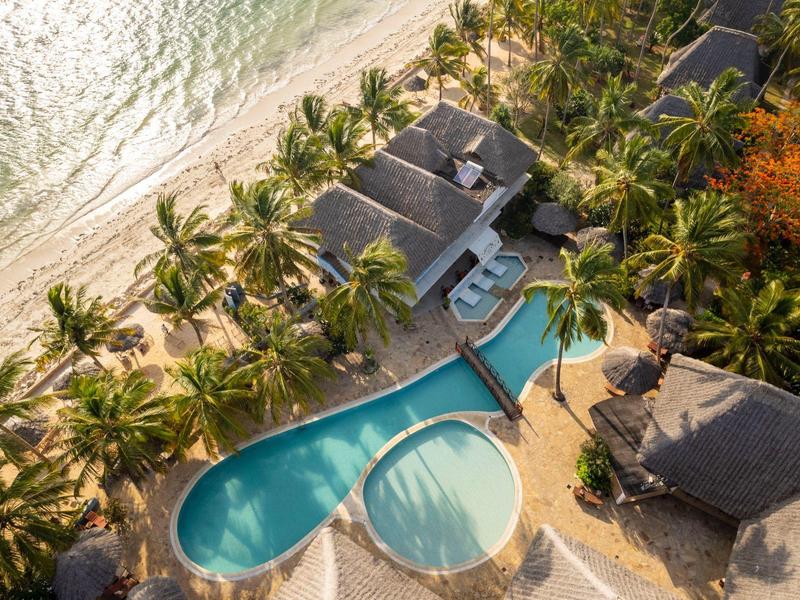 Luftaufnahme eines tropischen Resorts mit Pool, Palmen und Strand am klaren Meer.