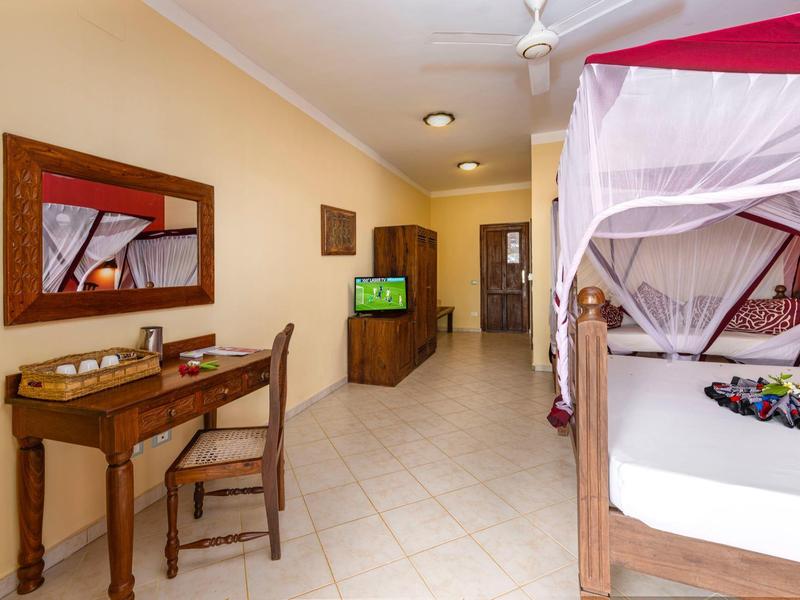 Helles Zimmer mit Holzmöbeln, Bett mit Moskitonetz, Flachbildschirm und Schreibtisch.