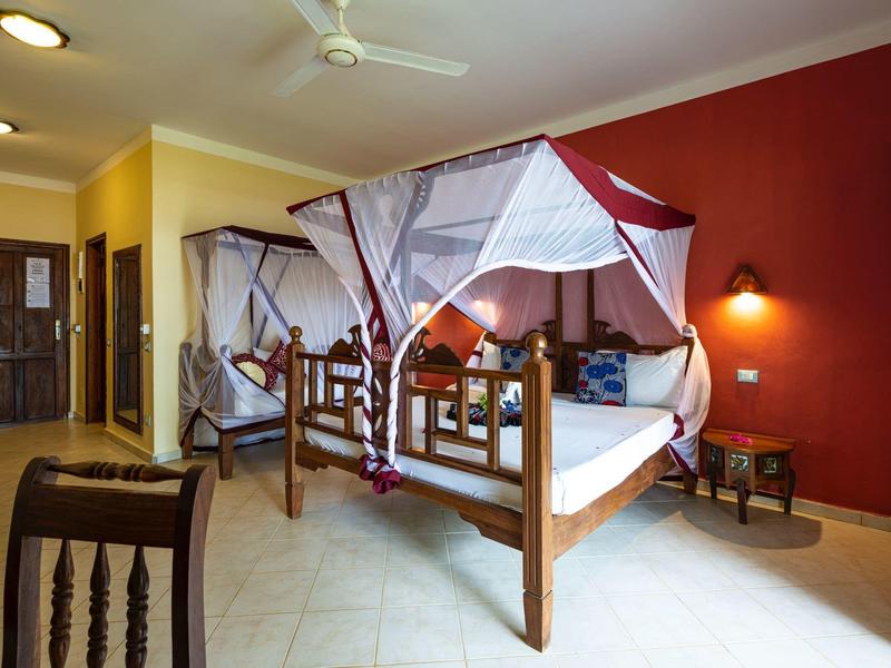 Hell eingerichtetes Schlafzimmer mit rustikalem Himmelbett, roten und gelben Wänden und dunklem Holz.