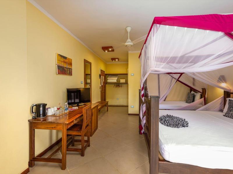 Ein helles Gästezimmer mit einem Himmelbett, Schreibtisch, Stuhl und Fernseher an der Wand.