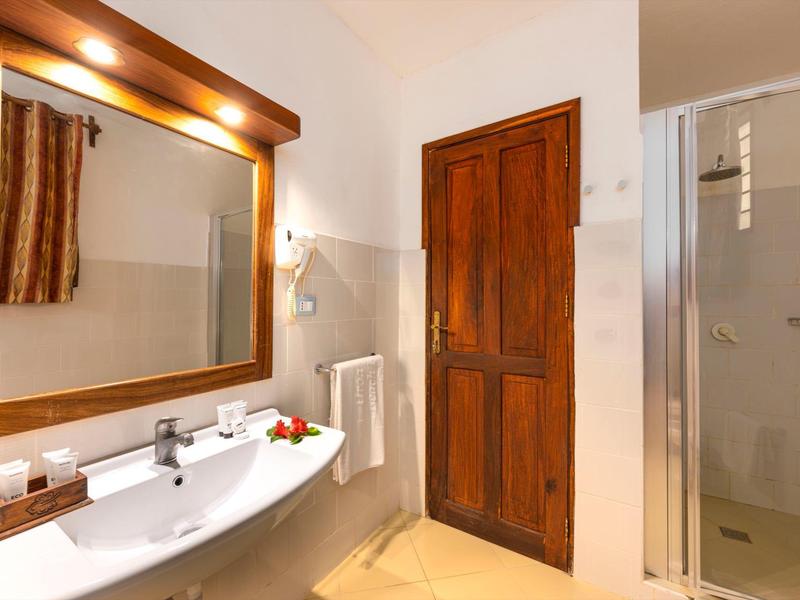 Helles Badezimmer mit Holztür, Glasdusche, großem Spiegel und weißem Waschtisch.