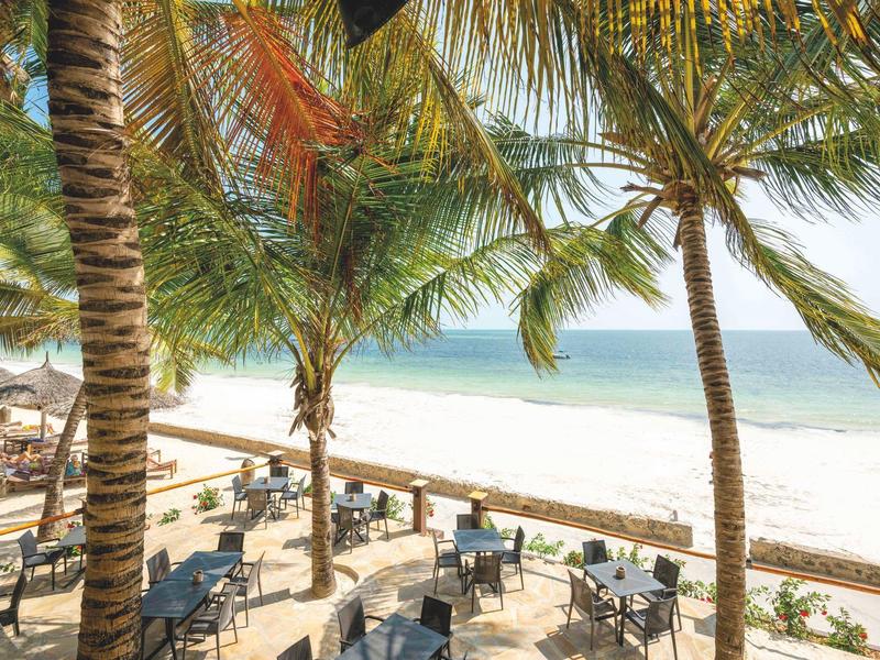 Restaurantterrasse am Strand mit Palmen und Blick auf das Meer bei klarem Himmel.