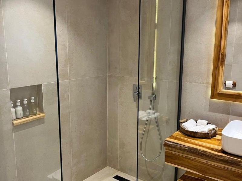 Moderne Dusche mit Glasabtrennung, grauen Fliesen und Holzregal mit Handtüchern und Waschbecken.