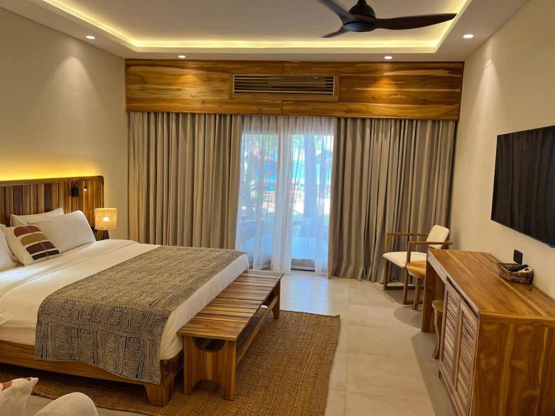 Helles Schlafzimmer mit Holzmöbeln, großem Bett, Teppich und geschlossener Gardine vor Balkon.