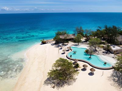 Strand mit weißem Sand, türkisfarbenem Meer und einem Pool mit Sonnenschirmen und Bäumen.
