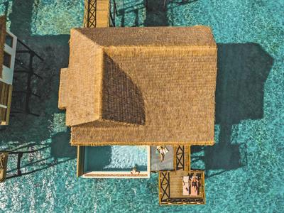 Letecký pohled na bungalov nad čistou vodou se sluneční terasou a bazénem