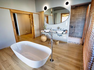 Moderní koupelna s volně stojící bílou vanou a světlou dřevěnou podlahou.