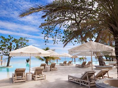 Plážový hotel s lehátky a slunečníky u klidného modrého moře pod modrou oblohou.