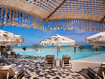 Pláž s deštníky, lehátky a výhledem na tyrkysové moře pod modrou oblohou.