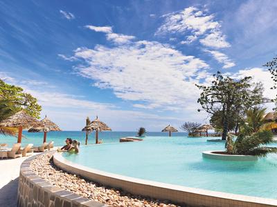 Infinity bazén s výhledem na moře a plážovými slunečníky pod modrou oblohou.