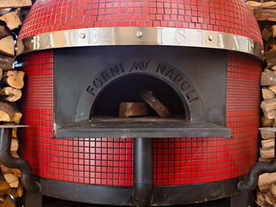 Červená pec na pizzu obklopená naskládaným dřevem.