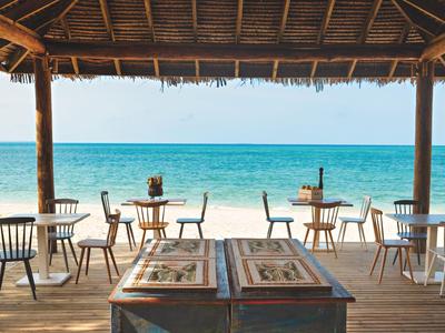 Otevřený plážový pavilon s stoly, židlemi a výhledem na moře pod modrou oblohou.