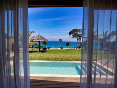 Výhled na bazén a zahradu směrem k moři z místnosti s průhlednými závěsy.